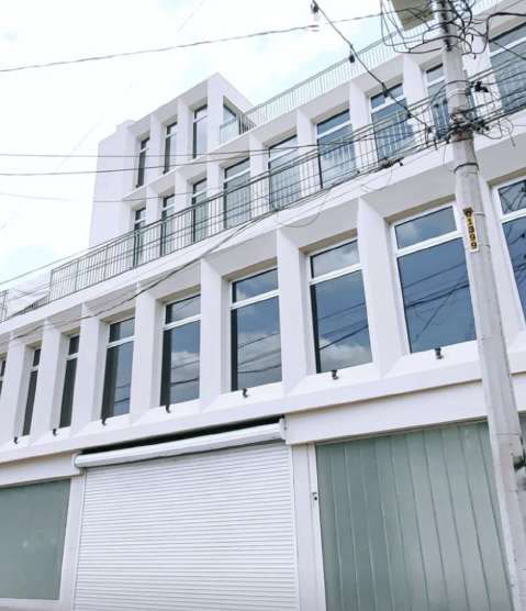 Street facade of D1AS: white vertical window bays, a roll-up door at grade, and a set-back terrace with a metal railing.