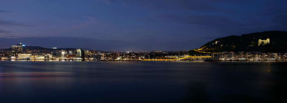 Night view of Oslo harbour with a glowing pedestrian path connecting the waterfront to Ekeberg hill.