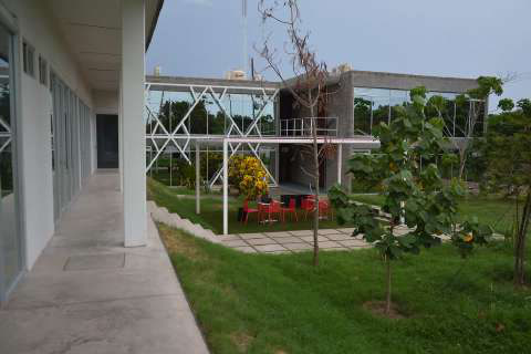 TARA courtyard with lawn, red chairs under a pergola, and a glazed wing with white steel X-bracing.
